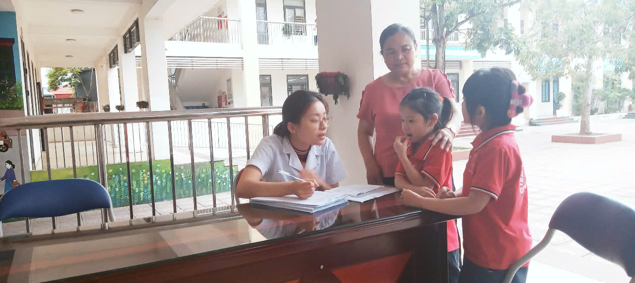 Cán bộ trạm y tế xã tiếp nhận giấy đăng ký của HS cùng cha mẹ HS