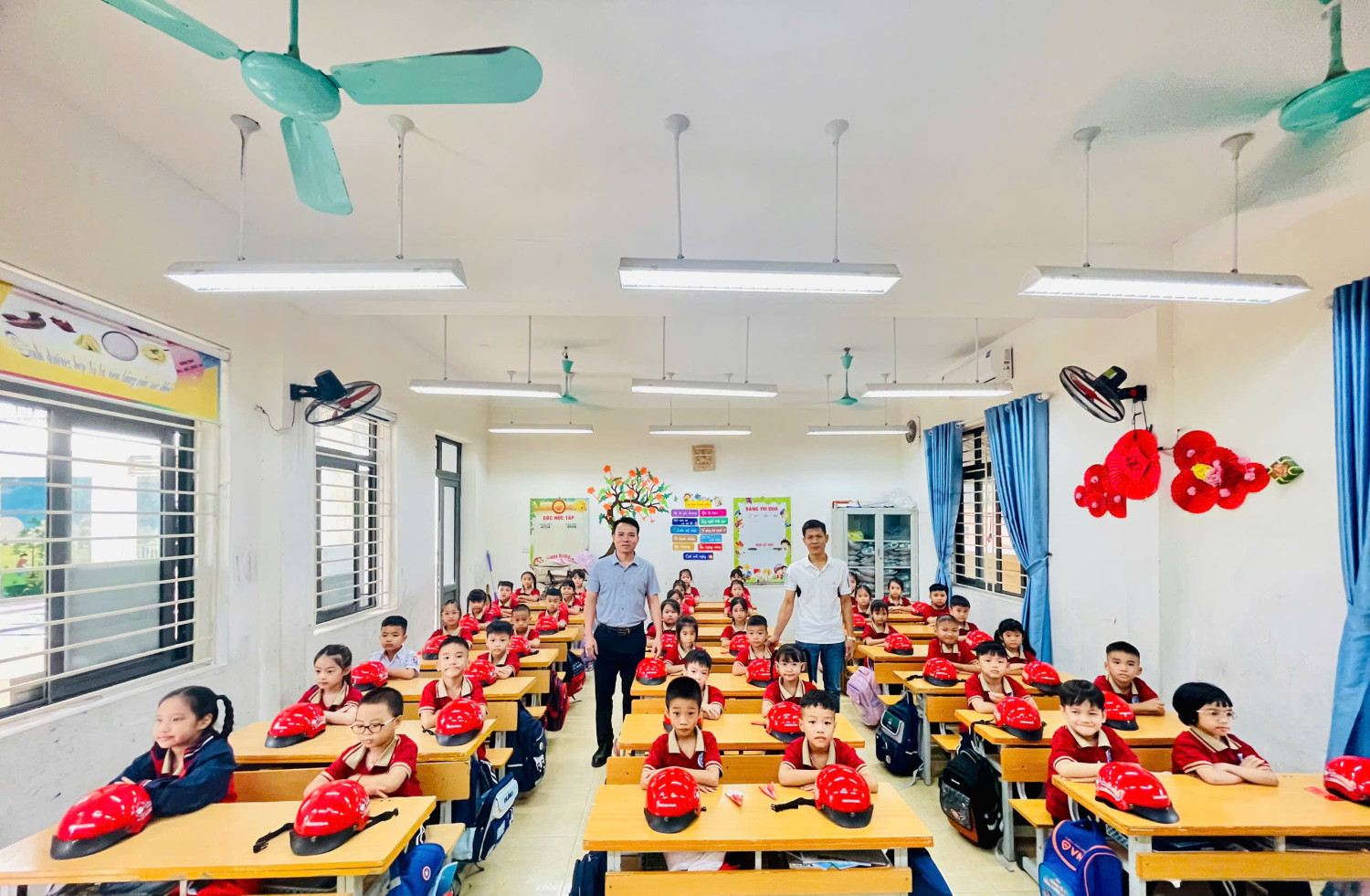 Thầy Hiệu trưởng Lê Quốc Bảo cùng thầy giáo Nguyễn Xuân Long trao tặng mũ BH cho học sinh lớp 1